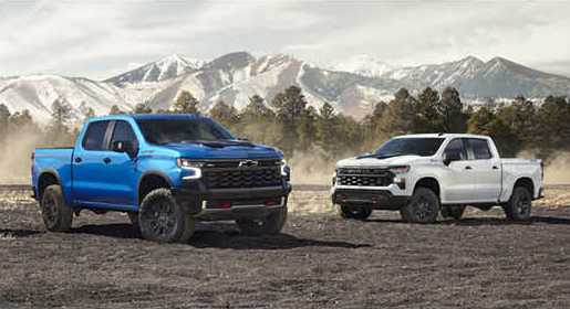 Chevrolet Silverado pickup trucks parked on rugged terrain with mountains in the background