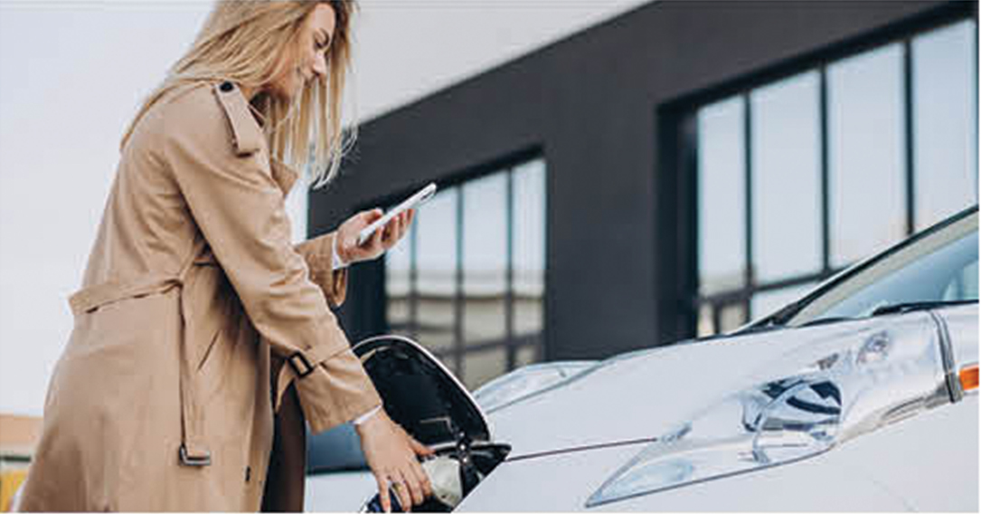 Woman charging an electric car while using a smartphone
