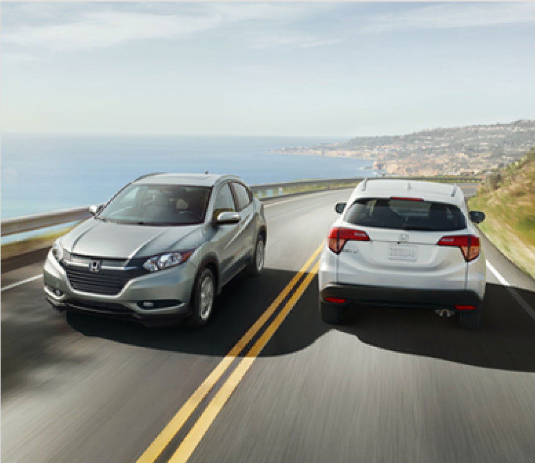 Two Honda compact SUVs driving side by side on a coastal highway