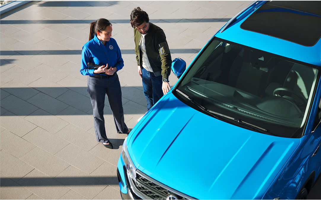 Volkswagen salesperson showing features on a blue SUV to a potential buyer at a dealership