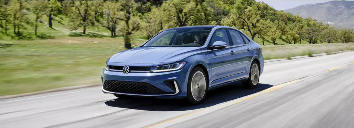 Blue Volkswagen Jetta sedan driving on a scenic country road