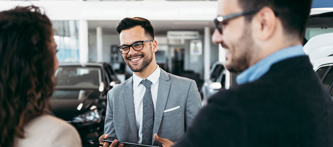 Car salesperson talking with customers inside dealership showroom
