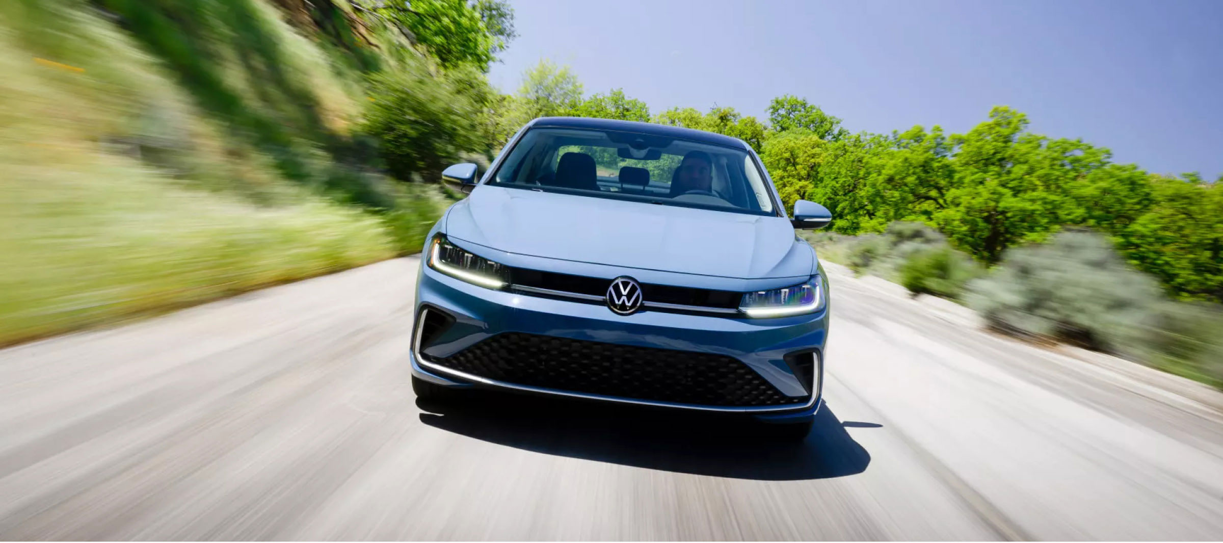 Blue Volkswagen sedan driving on a tree-lined road