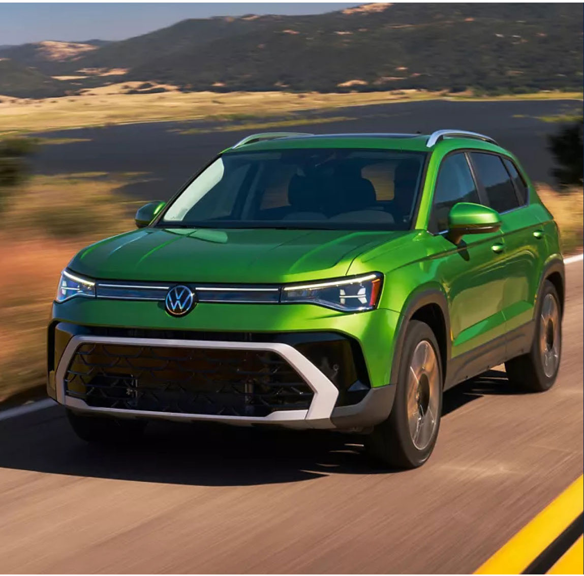 Green Volkswagen SUV driving on an open road with mountain scenery