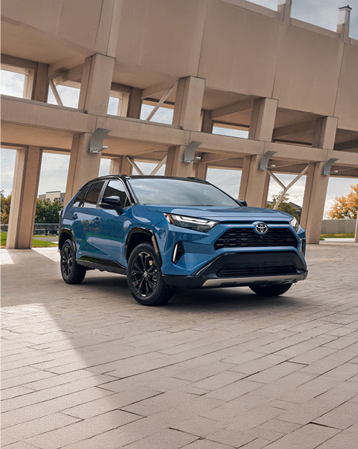 Blue Toyota RAV4 hybrid SUV parked near modern architecture