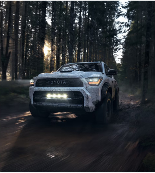 Toyota Tacoma driving through wooded trail with off-road lights on