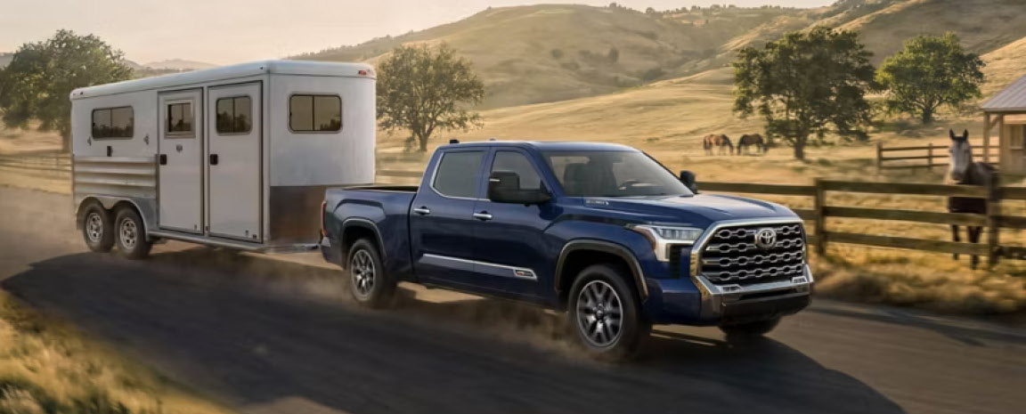 Blue Toyota Tundra towing a horse trailer through a rural countryside