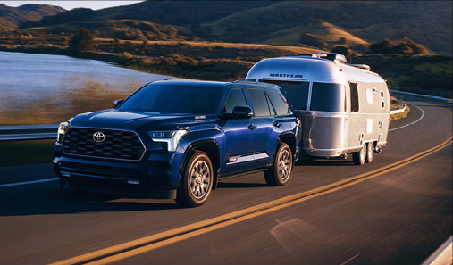 Toyota Sequoia SUV towing an Airstream travel trailer along a lakeside highway