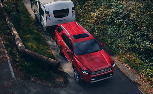 Red Toyota Sequoia towing a travel trailer on a wooded roadway