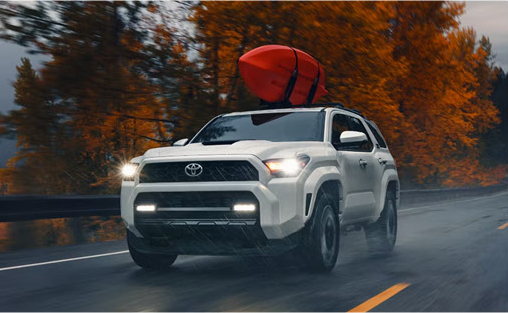 White Toyota 4Runner driving in rainy weather with a kayak mounted on the roof