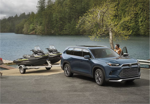 Toyota Grand Highlander towing personal watercraft on a trailer near a lakeside boat launch