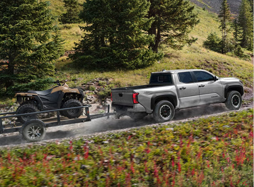 Toyota Tundra pickup truck towing an ATV trailer through a scenic mountain landscape