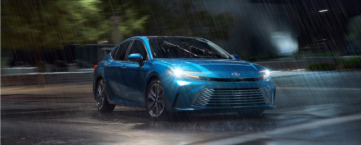 Blue Toyota Camry sedan driving through heavy rain at night with headlights illuminated