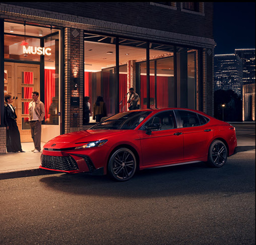 Red Toyota Camry parked outside a downtown entertainment venue at night