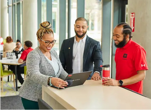 Three professionals collaborating around a laptop in a modern office environment