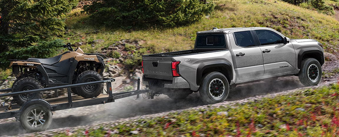 Toyota Tacoma towing an ATV trailer through rugged terrain showcasing towing capability, off-road confidence, and adventure-ready performance
