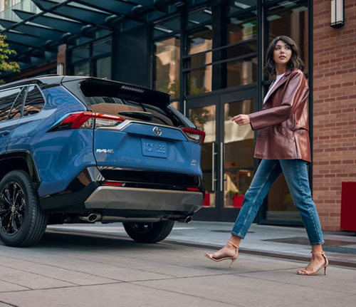 Woman walking past rear of blue Toyota RAV4 in city setting