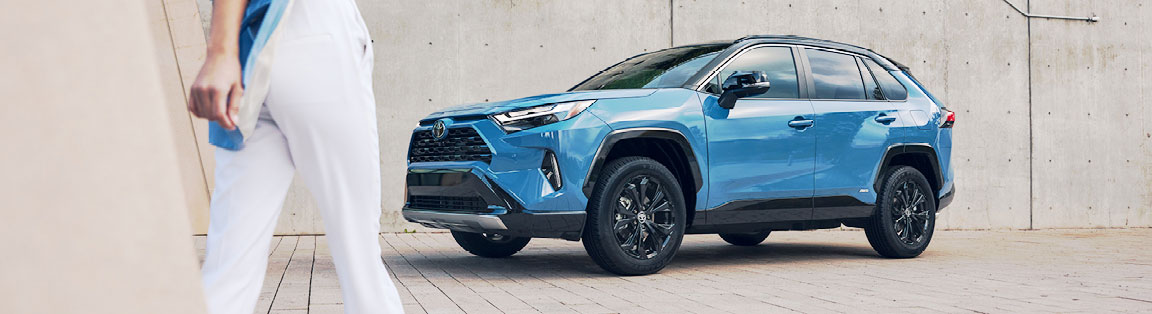 Blue Toyota RAV4 parked outside modern building with person walking nearby