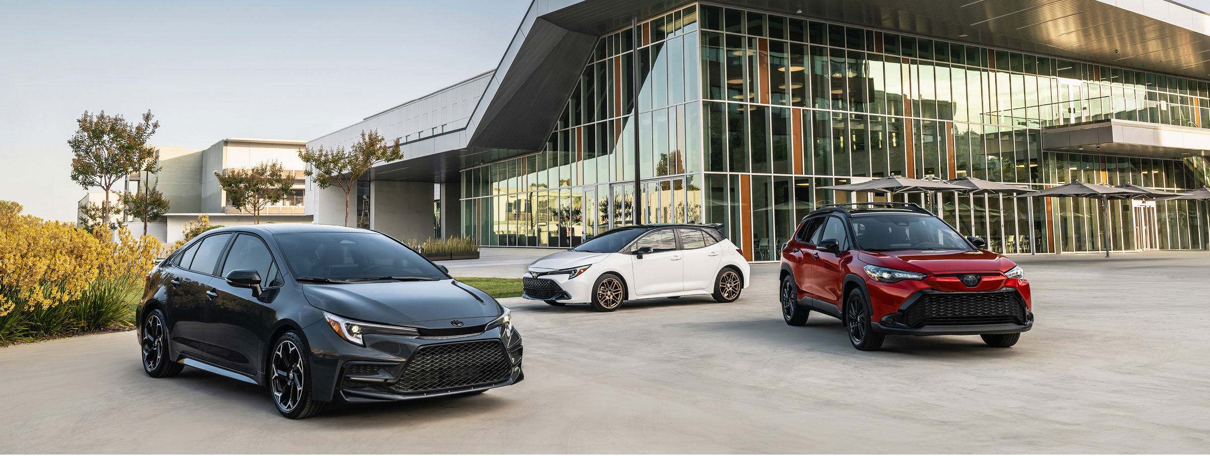 Toyota Corolla sedan, Corolla Hatchback, and Corolla Cross parked outside a modern building