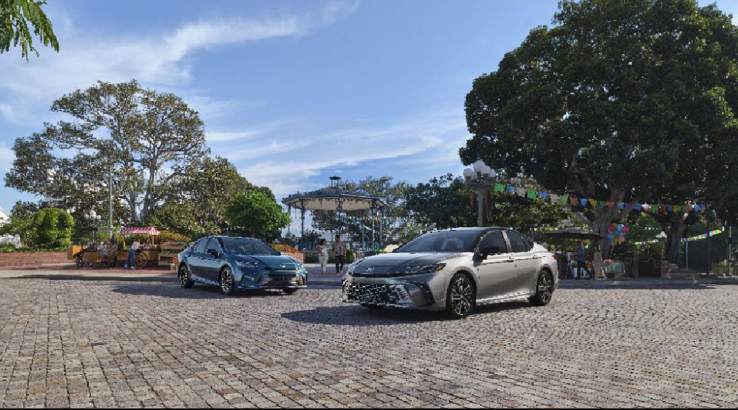 Toyota Camry sedans driving through a town plaza with outdoor market setting
