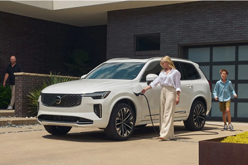 Family charging Volvo electric SUV at home driveway with wall charger