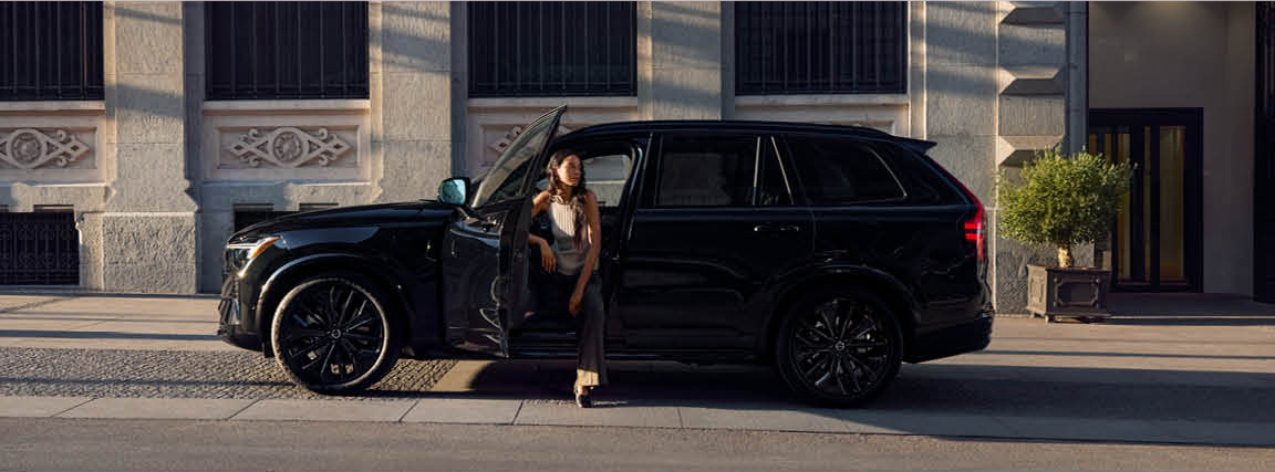 Driver stepping out of a black Volvo XC90 luxury SUV parked on a city street