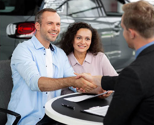 Customers shaking hands with dealership finance manager after car purchase