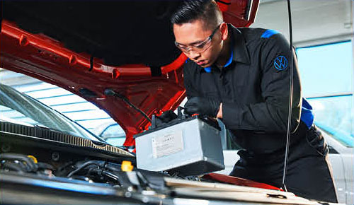 Volkswagen technician installing car battery under the hood