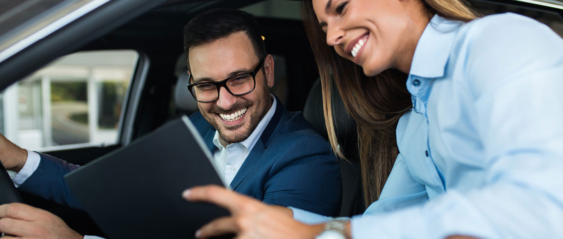car buyer reviewing features on tablet with sales representative inside vehicle at dealership