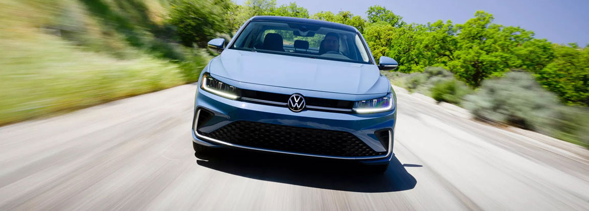 Volkswagen Jetta sedan driving on sunny road through green landscape