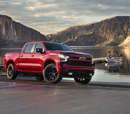 Red Chevrolet Silverado pickup truck parked near a boat ramp by a lake