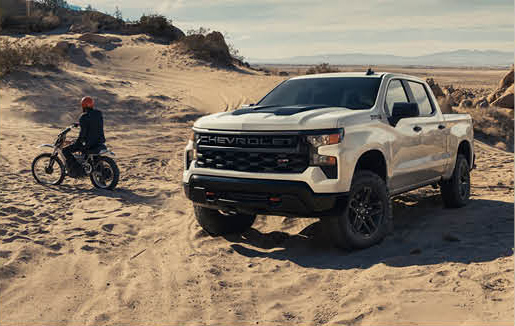 Chevrolet Silverado pickup truck parked in sandy off-road terrain with dirt bike nearby