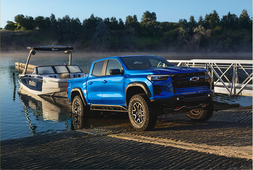 blue Chevrolet Silverado truck launching boat at lake ramp with trailer