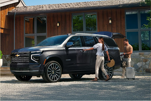 Chevrolet full size SUV parked outside modern home with couple unloading luggage