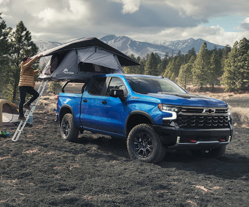 Chevrolet Silverado truck with rooftop tent camping in mountain forest setting