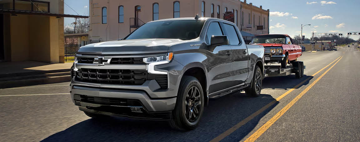Chevrolet Silverado pickup truck towing a classic car on a trailer through town