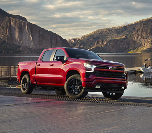 red Chevrolet Silverado pickup truck parked beside a lake near a boat ramp
