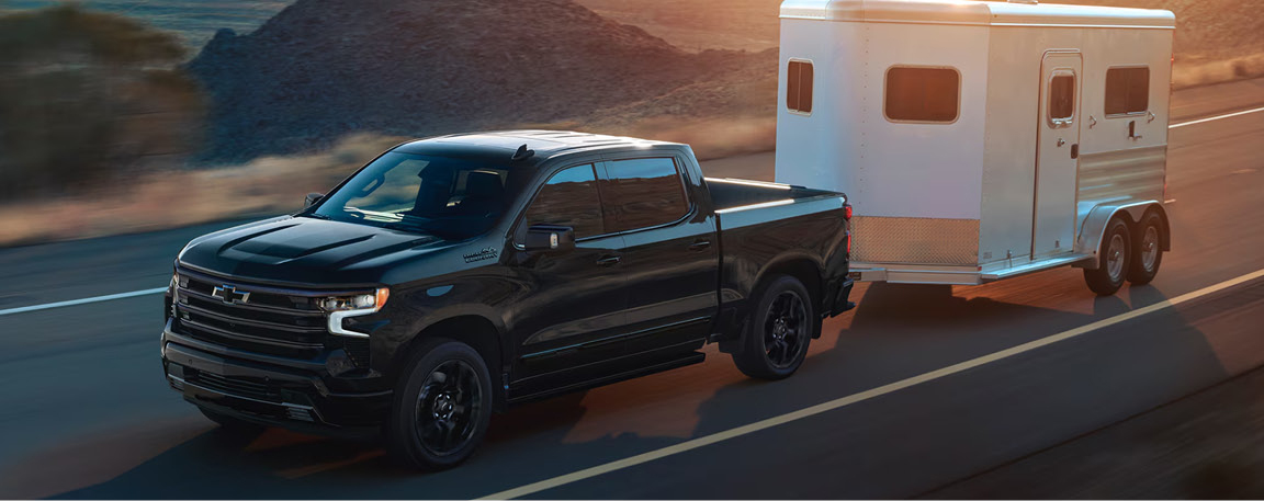 black Chevrolet Silverado pickup truck towing a horse trailer on an open highway