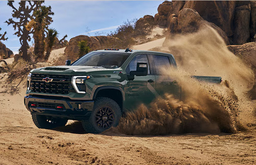 green Chevrolet Silverado HD ZR2 pickup truck powering through deep desert sand