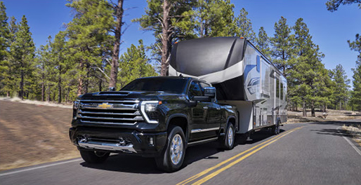 Chevrolet Silverado pickup truck towing a large fifth-wheel travel trailer on a forest highway