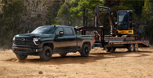 Chevrolet Silverado pickup truck towing a flatbed trailer carrying construction equipment