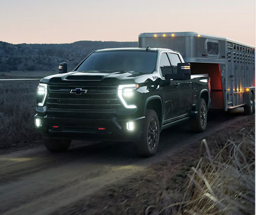 Heavy-duty Chevrolet Silverado towing a livestock trailer at dusk, demonstrating impressive towing power, work-ready capability, and dependable performance