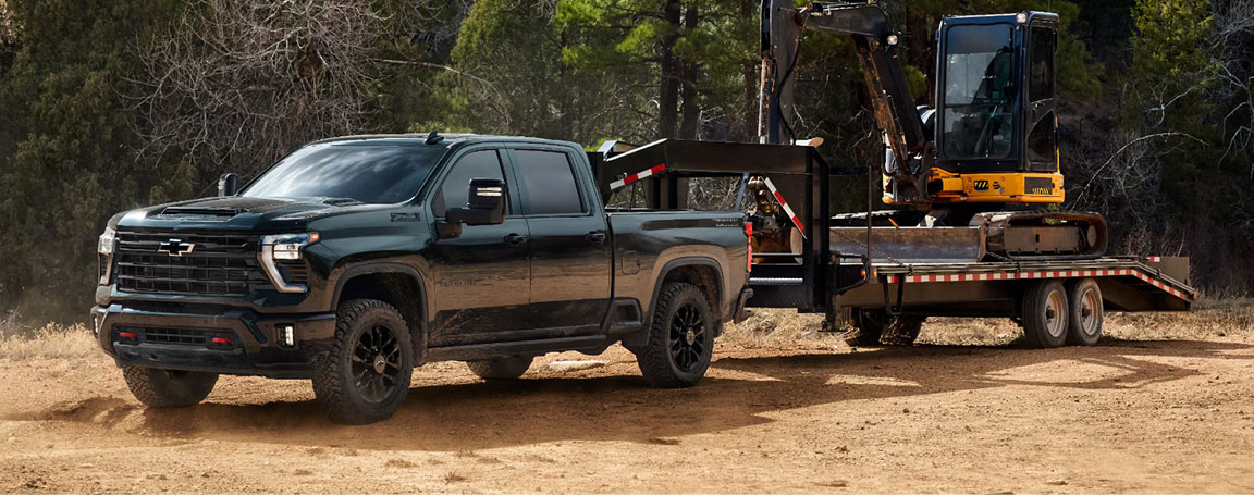 Chevrolet Silverado HD hauling heavy equipment on a flatbed trailer, highlighting maximum towing capacity, jobsite productivity, and commercial-grade strength