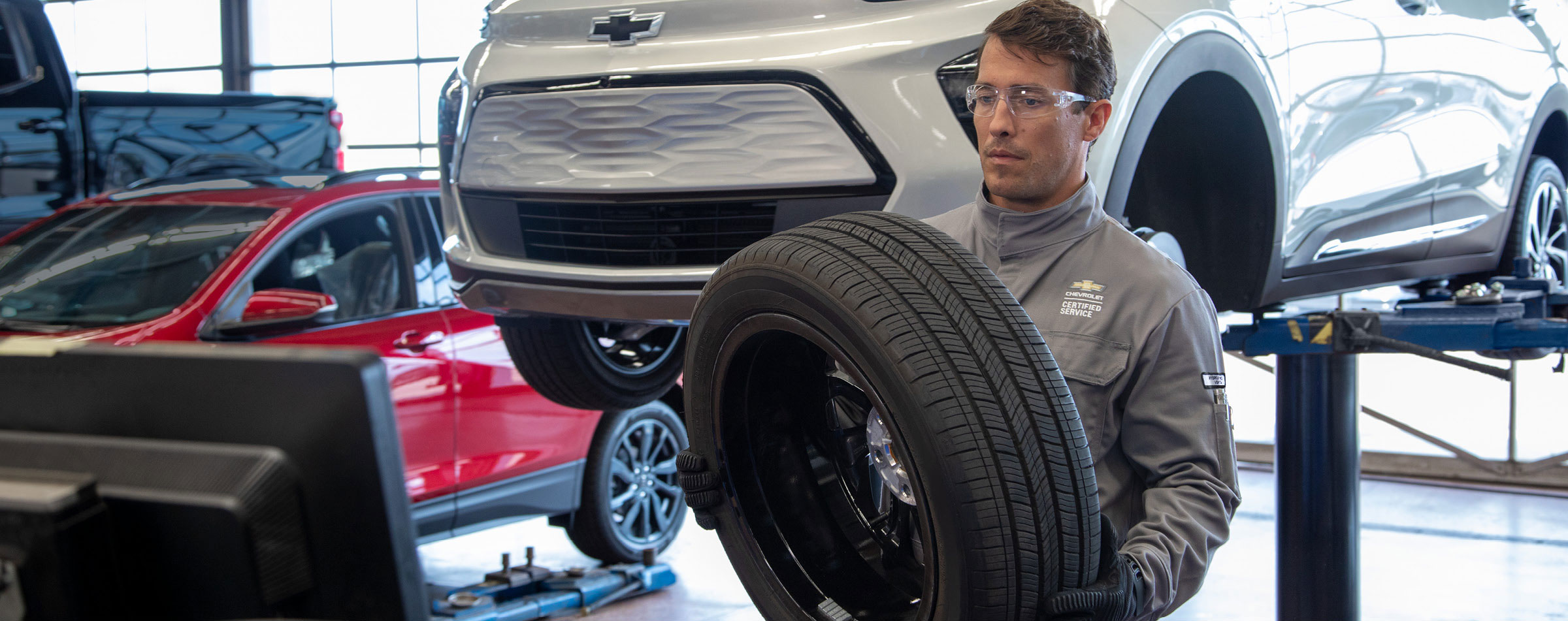 Chevrolet service technician inspecting and handling a vehicle tire inside a dealership service bay