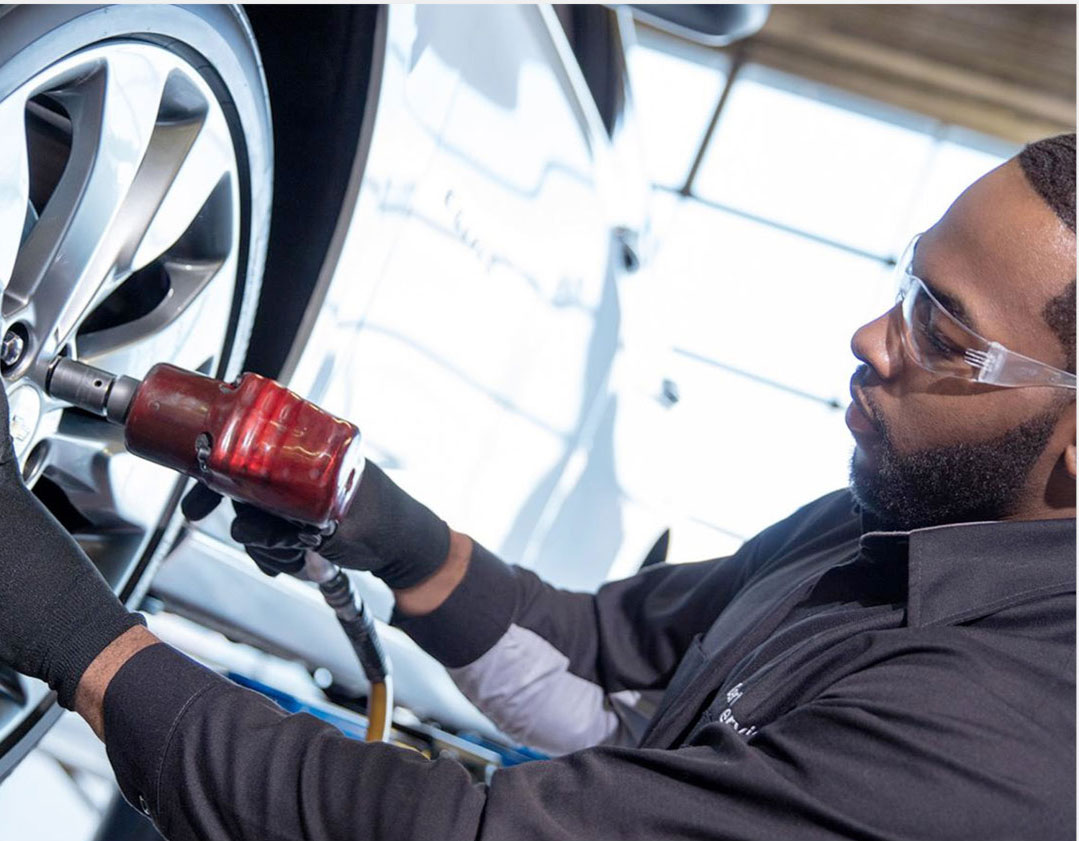 Automotive technician using a power tool to remove a wheel during a wheel alignment service