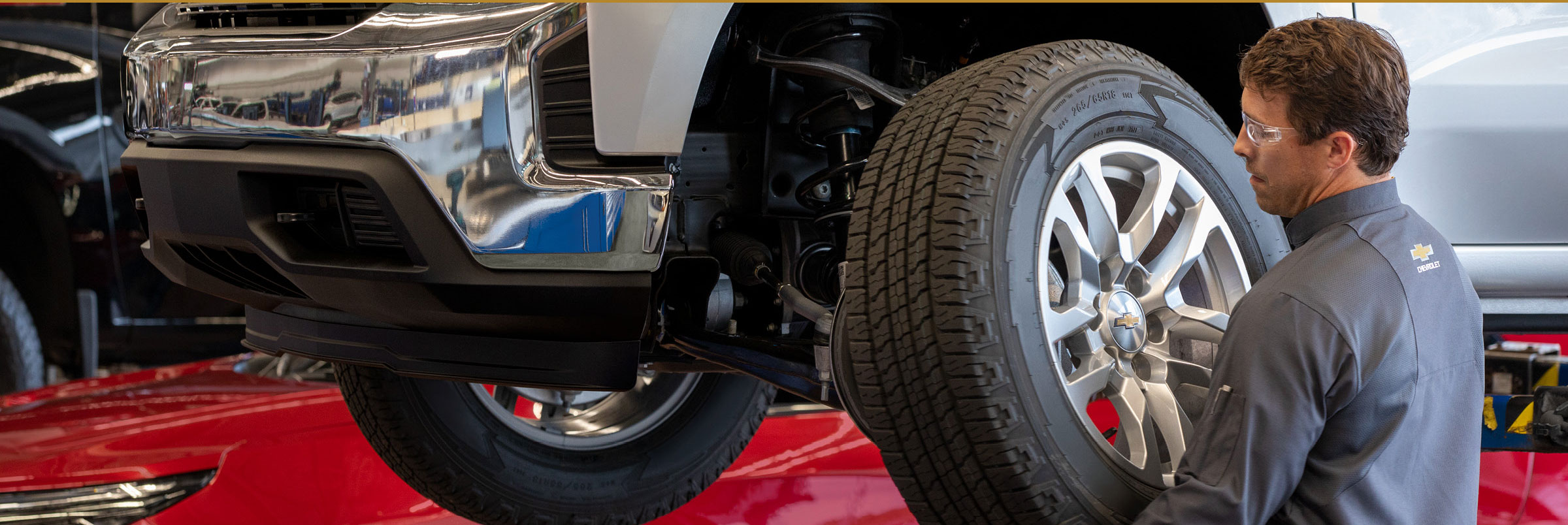 Chevrolet service technician performing wheel alignment work on a lifted vehicle in a service center