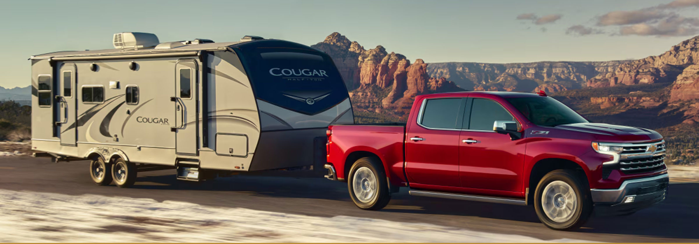 Red Chevrolet Silverado towing a travel trailer through desert scenery
