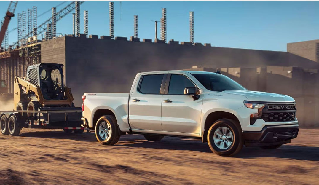 White Chevrolet Silverado towing construction equipment at a job site